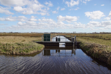 Very small Dutch weir (Dutch: klepstuw) in a ditch. The weir regulates the water drainage capacity of the surface water body. Late winter, meadows, March. Netherlands.