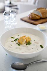 Bowl of Clam Chowder with Whole Grain Bread on a White Kitchen Counter