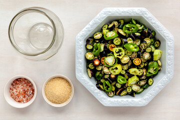 Bowl with cut spicy peppers (various cultivars) and other ingredients to make sliced pickled chillies, top view.