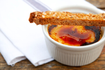 Crème brûlée in a white ramakin with a crouton in a restaurant