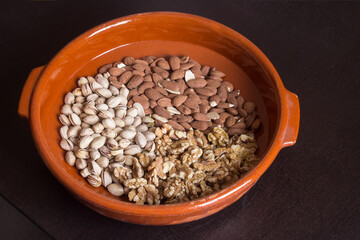 A group of walnuts, pistachio, and almonds scattered neatly on a wooden casserole on a dark table. Variety of nuts.