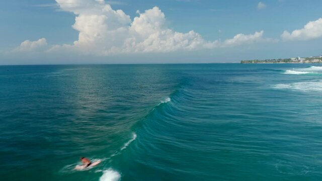 Aerial view of people surfing across the waves in tropical blue ocean. Fast wave breaking across the ocean surface