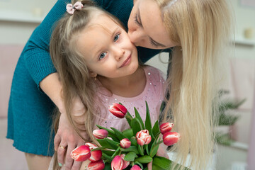 mom bending over her daughter, kissing her on the cheek. daughter holding a bouquet of fresh spring tblps in her hands. mothers day, womens wives