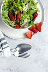Salad with lettuce, strawberries, red onion, corn; olive oil and walnuts