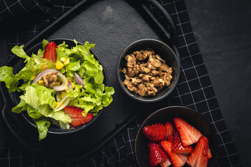 Salad with lettuce, strawberries, red onion, corn; olive oil and walnuts