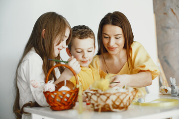 Children paint eggs. Mother teaches children. Sitting at a white table.
