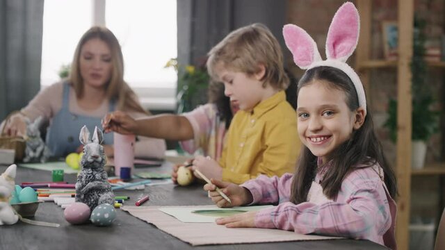 Portrait of happy girl in bunny ears headband making Easter card in arts and crafts class, then smiling for camera