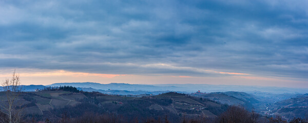 Italy Piedmont: panoramic winter snow view wine yards unique landscape at sunset, medieval castle and village on hill top, the Alps in the background dramatic sky