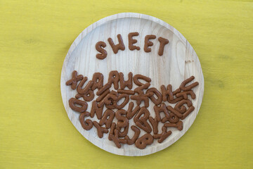 alphabet biscuits and the word sweet on a wooden plate yellow background