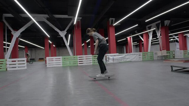 Young woman performs a nice kickflip at indoor skatepark.