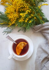 Still life with a bouquet of mimosa and tea with lemon on a gray background