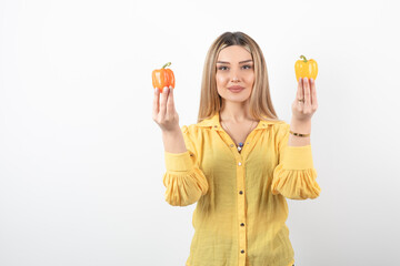 Portrait of positive woman holding colorful bell peppers over white wall