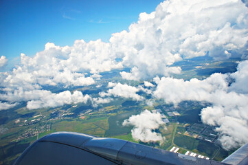 Fototapeta na wymiar Beautiful snow white clouds and aerial view of the green lands from the window of the airplane and part of the wing of plane, flight, journey, travel, cloudscape, sky overcast
