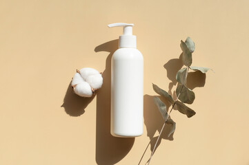 Beauty SPA branding mock-up. Natural organic eco cosmetics. White cosmetic bottles, cotton flowers, eucalyptus leaves with sun shadows on beige background flat lay top view. Blank label for branding