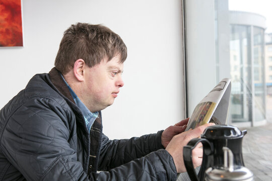 Man with down syndrome reading newspaper by cafe window