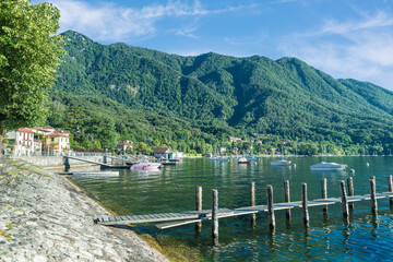 Fototapeta na wymiar Fascinating glimpse of a large Italian lake with moored boats and a jetty in the foreground. Lake Maggiore at the village of Caldè (Castelveccana), northern Italy 