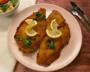 Golden breaded plaice fish fillet with potato salad and lemon.