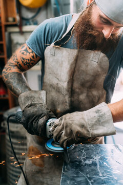 Axe maker using steel grinder in workshop