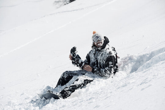 Male snowboarder covered in snow sitting on mountainside, Alpe-d'Huez, Rhone-Alpes, France