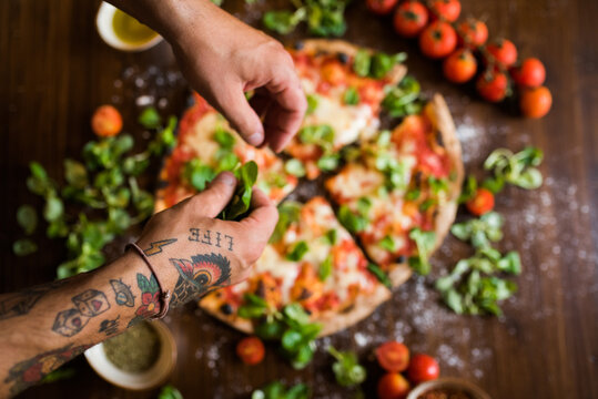 Chef garnishing pizza with basil leaves on kitchen worktop