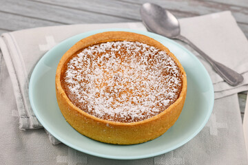 Small whole traditional European cheesecake topped with powdered sugar on light blue plate