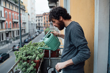 Bearded young man watering plants on balcony
