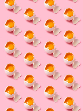Broken eggs arranged in rows on pink background