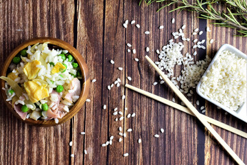 On a rustic table, rice three delights, in a wooden bowl, accompanied by long chopsticks