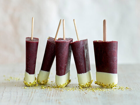 Tri-coloured ice lollies in a row on table, white background