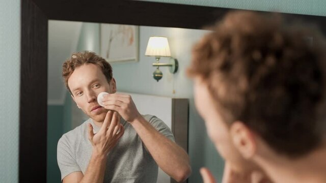 A handsome man wipes his skin with a cotton pad