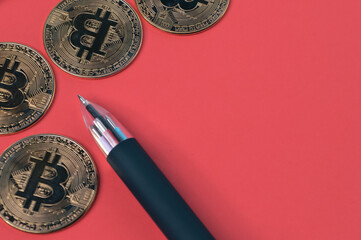 Golden bitcoins and pen over red background.