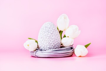 Grey easter egg in the nest and white tulips on a pink background