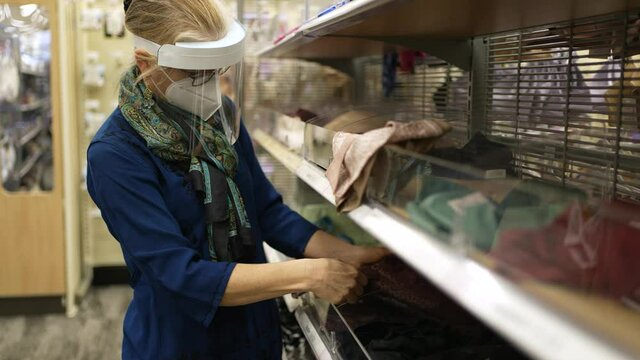 Close up woman wearing face shield and mask shopping for clothes in a store. Female with PPE personal protection equipment buying at shopping mall center coronavirus pandemic.