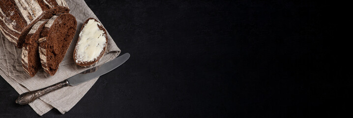 Freshly baked homemade artisan sourdough rye and white flour bread. Sliced. Bread and butter and vintage table knife on dark background. Banner. Copy space.
