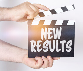 On a white background, a man holds a clapperboard in his hands on which it is written - NEW RESULTS