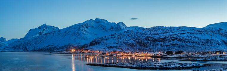 A quiet afternoon in the harbor with ships in a fishing village, where in the background you can see the peaks of the mountains and bridges linking the islands in Lofoten.