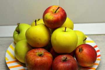 A heap of apples in a plate on the table. Red and green juicy ripe apples lie in a slide on a white plate against the background of a gray wall. Stock photography fruit top view