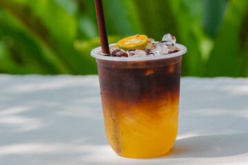 Iced Coffee with kumquat in a Takeout glass on green nature background, Eat a black coffee or americano reduce sweeteners in beverages and foods, A healthy diet drink.