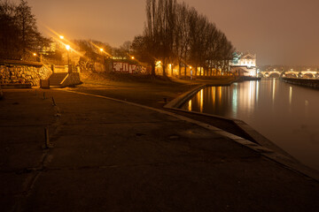 Vltava river bank after sunset and in the background blurred Charles Bridge in Prague