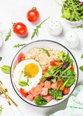 Savory breakfast. Oatmeal porrige with salmon fish, egg and fresh salad. Healthy food, balanced nutrition. Top view on white table.