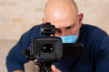 Man wearing face mask, looking to view finder of the camera and filming