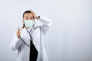 Woman doctor in white uniform wearing a medical mask and holding stethoscope