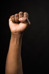 Raised fist of a black man, on black background.