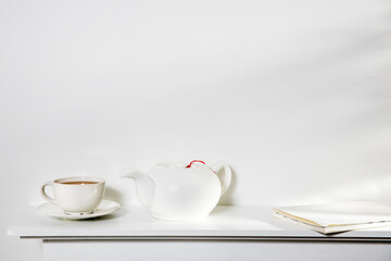 White on white. A cup of tea, a kettle, and a notebook stand on a white panel of an artificial fireplace.