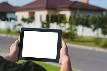 A tablet in the hands of a man, against the backdrop of a house.