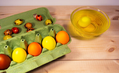 There is a container with colored eggs on a wooden table. Eggs lie in bowls with dyes.