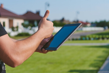 Finger in front of the Tablet on the background of the house.