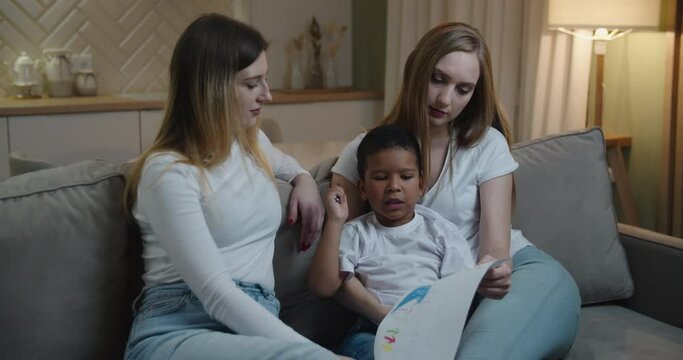 Mother and aunt Europeans help their little African American son draw. International family. High quality 4k footage
