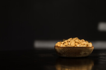 Roasted peanuts in wooden bowl on black background with tabletop refelction