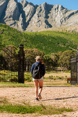 Young Latin woman hitchhiking on the road with a backpack waiting for someone to give her a ride in the mountains and forests on a sunny day.